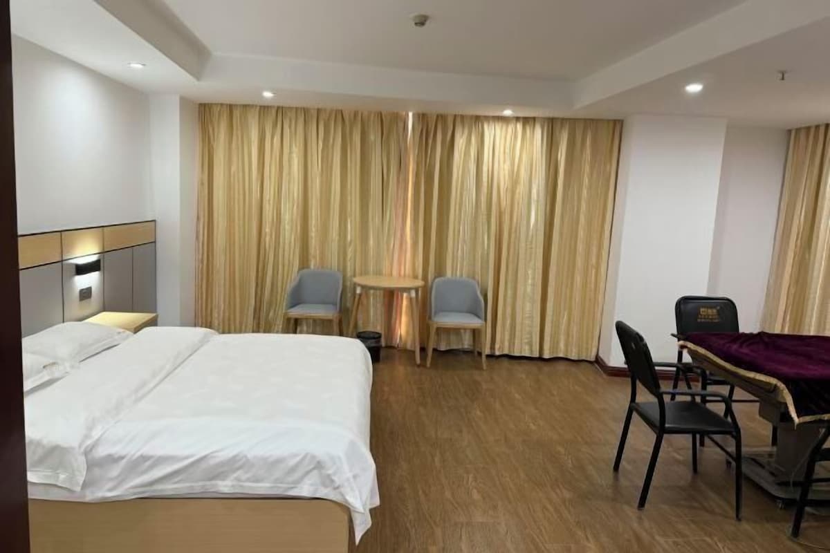 Habitación de hotel con una cama, un escritorio con una silla, una mesita pequeña y dos sillas.