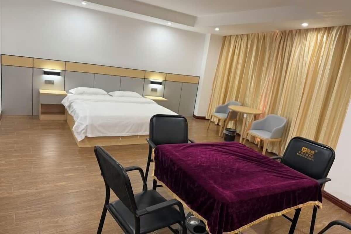 Quarto de hotel com cama, mesas de cabeceira, escrivaninha e cadeiras, e cortina.