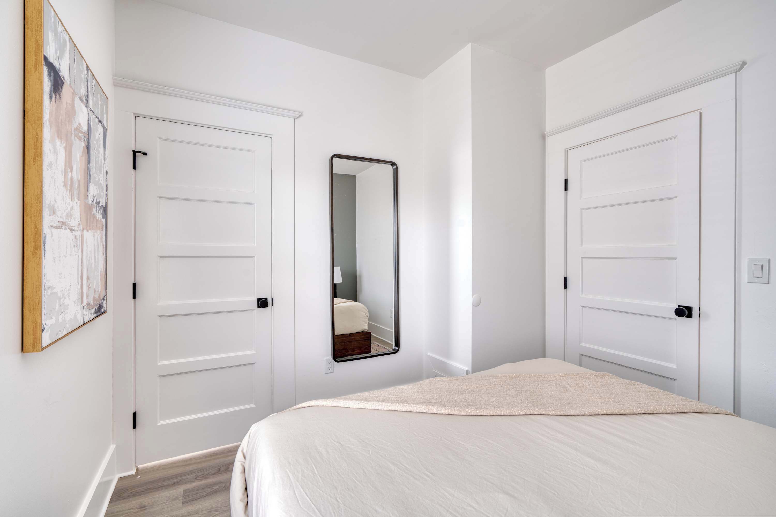 A bedroom with a bed, a mirror, and two white doors.
