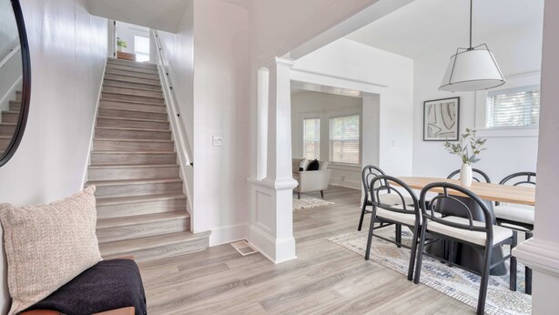 Amplia sala de estar con escalera de madera, comedor con mesa y sillas, y un ventanal con persianas.