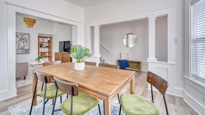 Un comedor con una mesa de madera, sillas con cojines verdes, una planta en maceta y una escalera que lleva a otra habitación.
