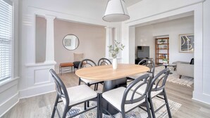 Een eetruimte met een ronde houten tafel, zwarte stoelen, een witte vaas en een hanglamp.
