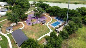 Luchtbeeld van een park met speeltoestellen, tennisterreinen en een rivier op de achtergrond.