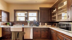 A kitchen with wooden cabinets, a stainless steel dishwasher, a microwave, and a window above the sink. - Historic Craftsman | 5BR/2BA | Foodie Row (Portland)