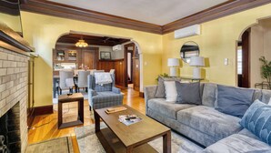 A living room with a fireplace, a sofa, a coffee table, and a dining area with chairs and a table. - Historic Craftsman | 5BR/2BA | Foodie Row (Portland)