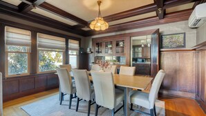 A dining area with a wooden table and chairs, a chandelier, and large windows with blinds. - Historic Craftsman | 5BR/2BA | Foodie Row (Portland)