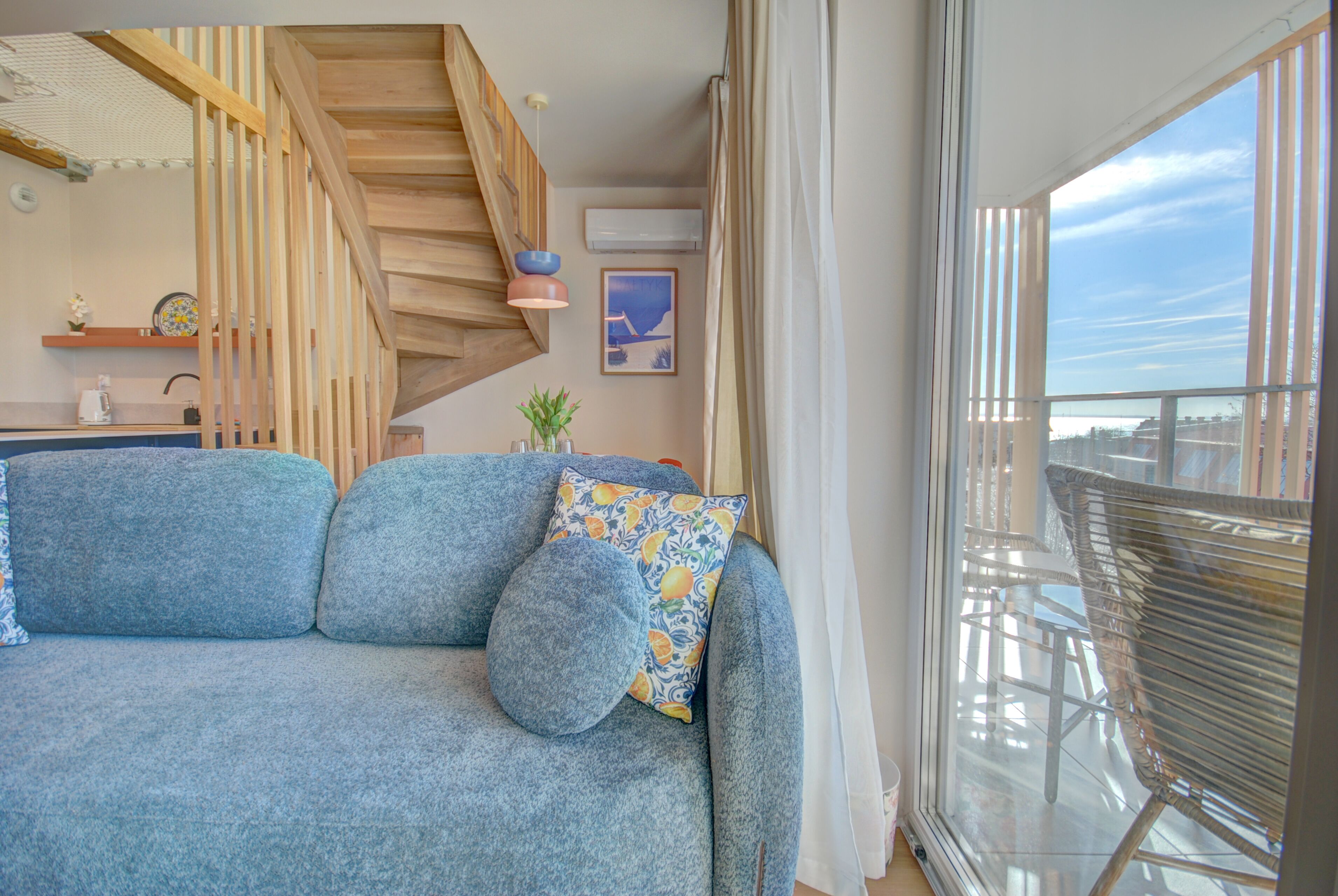 A living area with a sofa, a staircase, a dining table, and a view through a large window.