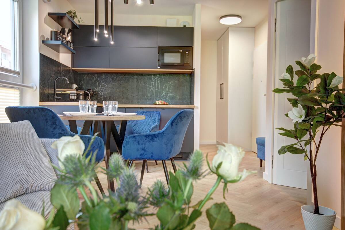 Una cucina moderna con mobili scuri, un forno a microonde e un'area pranzo con sedie blu e un tavolo rotondo.