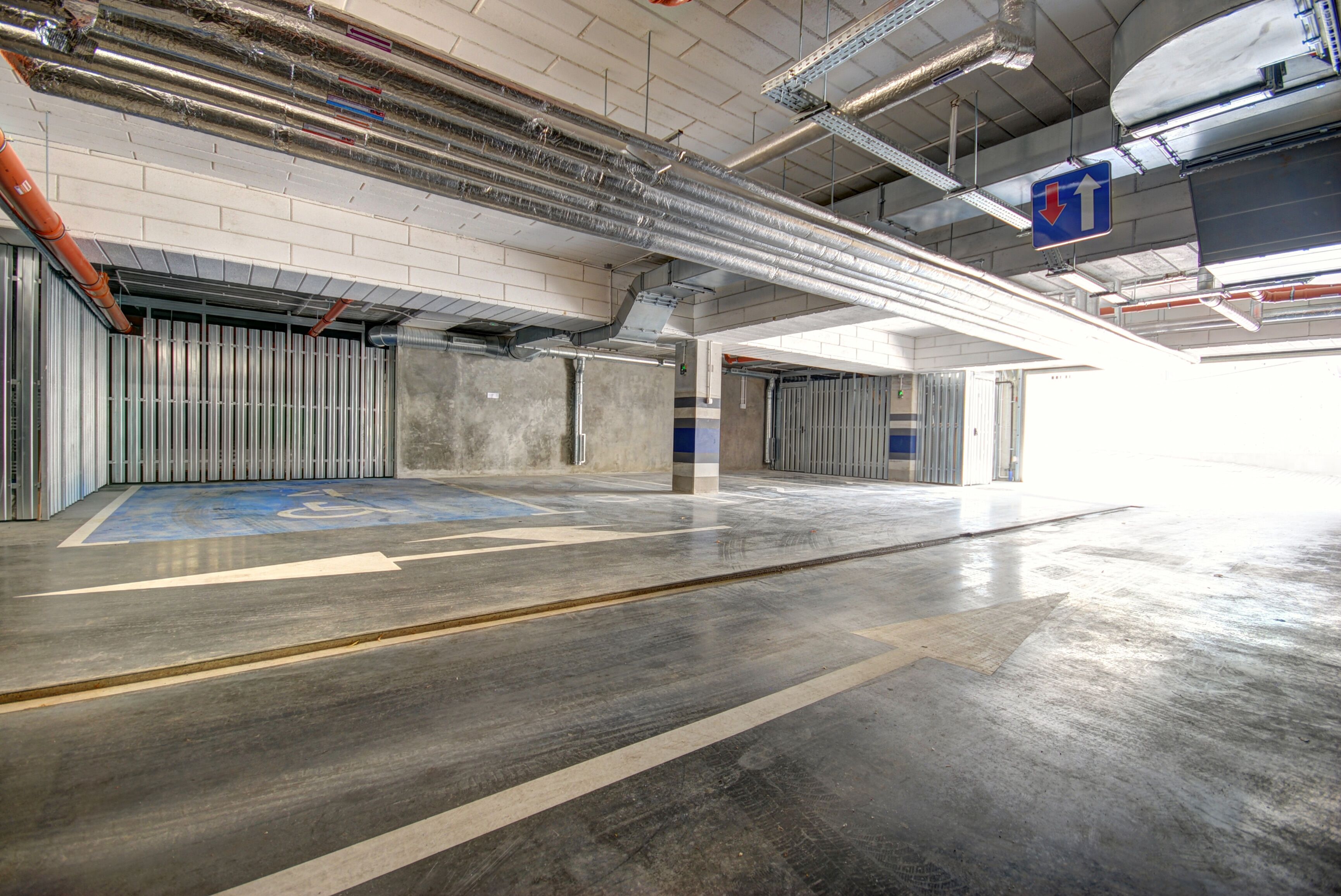 A spacious indoor parking area with clear directional signage, a wheelchair-accessible ramp, and a clean, well-lit environment.