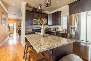A kitchen with dark wooden cabinets, a stainless steel refrigerator, granite countertops, and a vase with flowers on the island.
