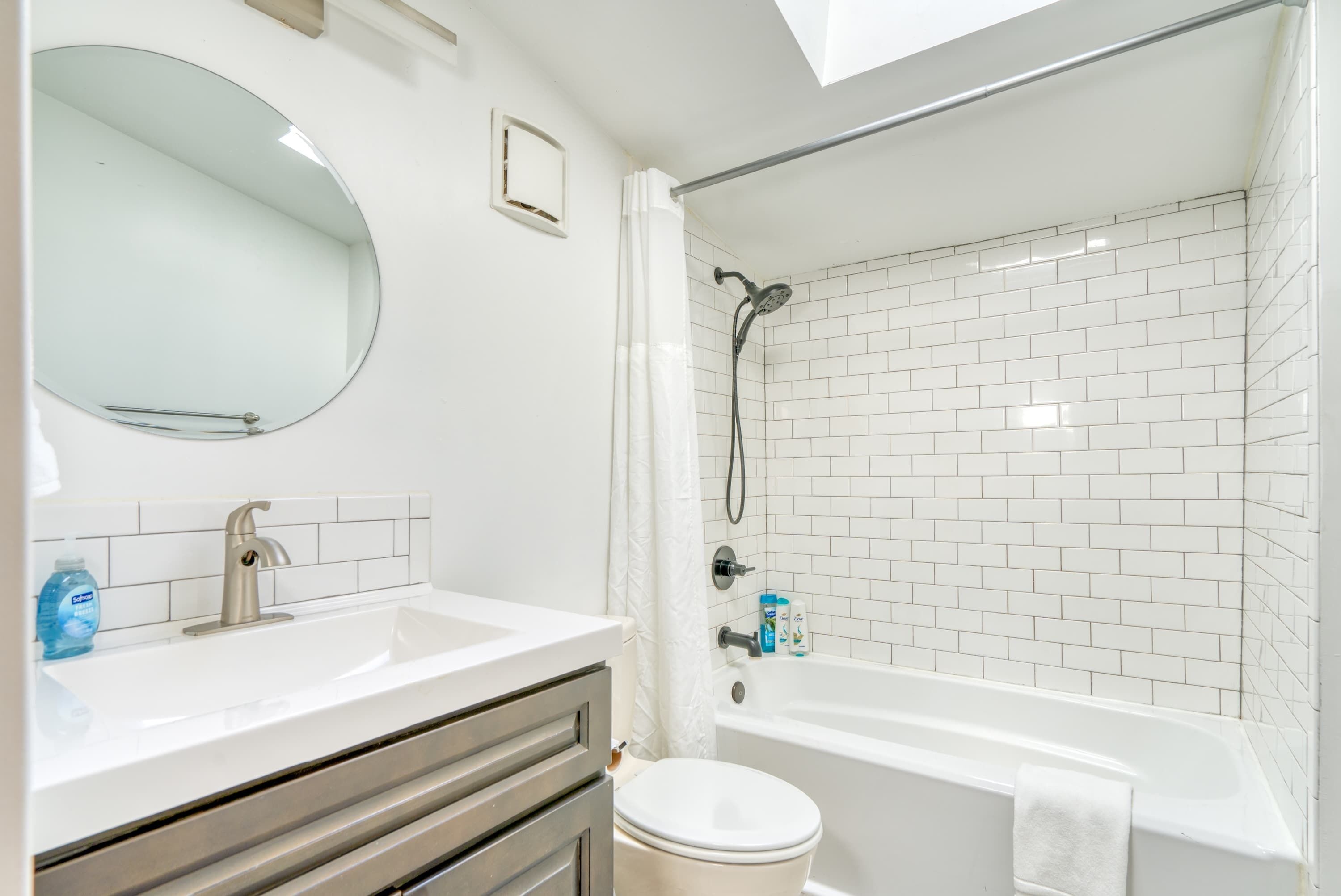 A bathroom with a white sink, mirror, and white-tiled shower area.
