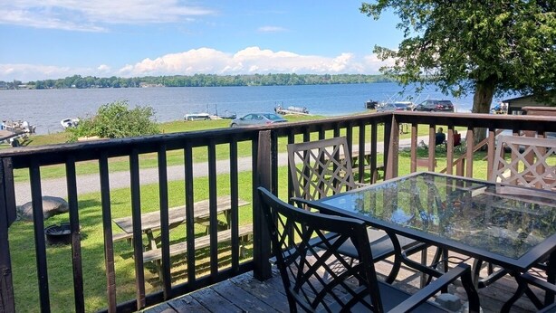 Una terraza con mesa y sillas de vidrio, con vista a un lago con botes y un muelle.