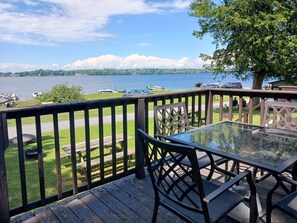 Una terraza con mesa y sillas de vidrio, con vista a un lago con botes y un muelle.