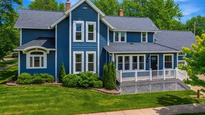 Ein blaues, zweistöckiges Haus mit Veranda, Schornstein und gepflegtem Rasen.