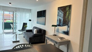 A modern living room with a sofa, a dining table, and a desk. There are two paintings on the wall and a chair with a vase of flowers. - Excellent connections to the trade fair, cathedral and old town by public transport, yet in a very quiet location  (Köln)