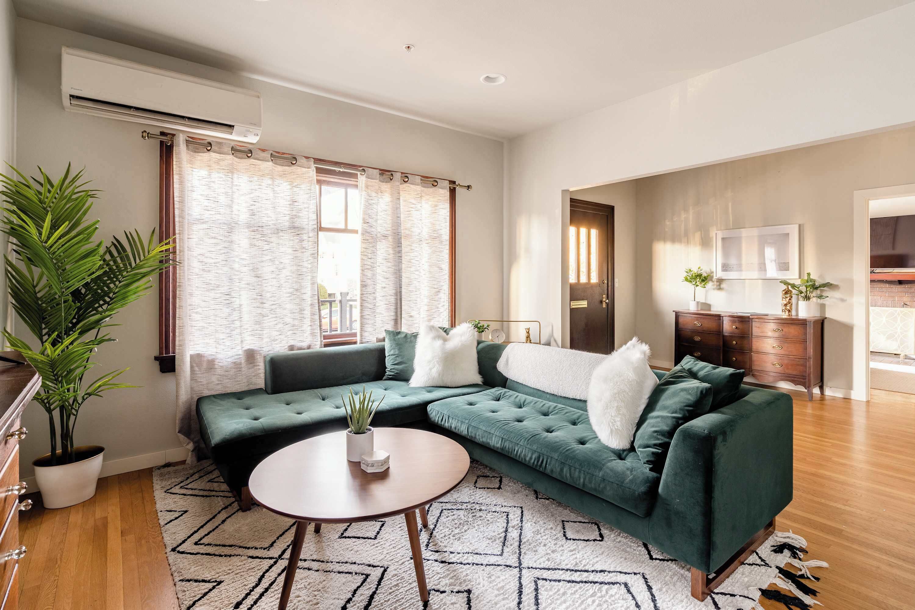 Een woonkamer met een hoekbank, een ronde salontafel en een potplant.