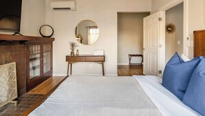 A bedroom with a large bed, a wooden dresser, a round mirror, and a door leading to another room. - 8BR/5BA Compound | 3 Kitchens | Sleeps 16 (Portland)