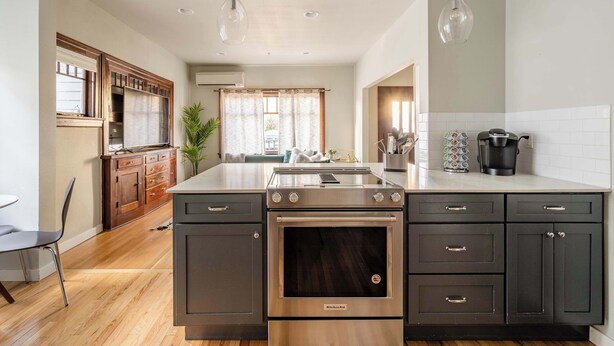 A modern kitchen with a central island, dark cabinetry, stainless steel appliances, and pendant lighting.