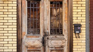 A weathered wooden door with a metal gate, a mailbox with the number 124, and a brick wall.