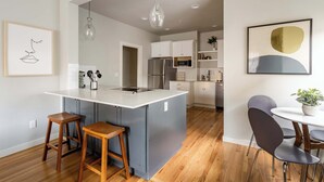 A modern kitchen with a central island, wooden stools, a dining table with chairs, and a hanging light fixture.