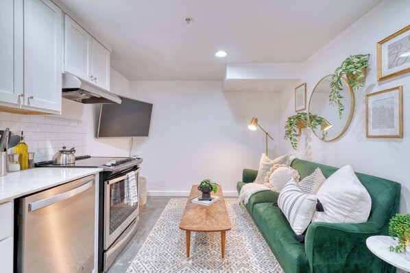 Une cuisine compacte dotée d’appareils électroménagers modernes, un canapé vert et une petite table basse.