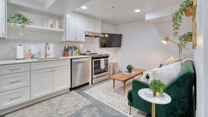 A compact kitchen with white cabinets, a built-in oven, and a sink. There is a green sofa and a small table with a plant. - Retro Hideaway - Trendy Location - 2BR - Sleeps 4 (Portland)