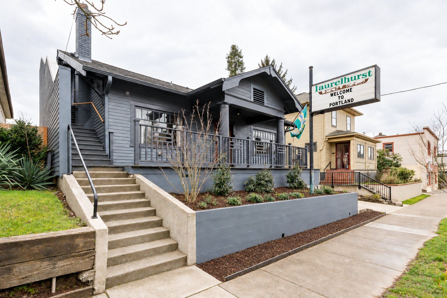 Una casa de dos pisos con un porche delantero, una escalera que conduce a la entrada y un letrero dando la bienvenida a Portland.