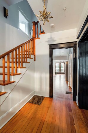 A wooden staircase leading to a balcony with a view, a modern ceiling light, and a clean, well-lit interior.