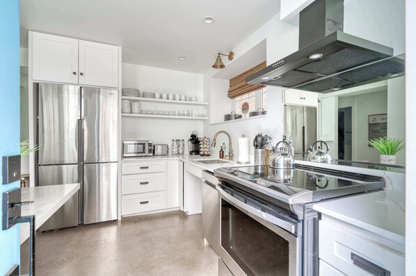 Una cocina moderna con electrodomésticos de acero inoxidable, armarios blancos y una isla central con hervidor.