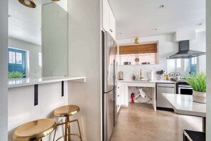 Una cocina moderna con un refrigerador de acero inoxidable, armarios blancos, una persiana de madera y una planta en maceta sobre la encimera.