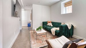 A modern living room with a green sofa, a coffee table with a plant, and a large window with a view. - 1906 3BR Retreat • NW 23rd Boutiques & Eats (Portland)