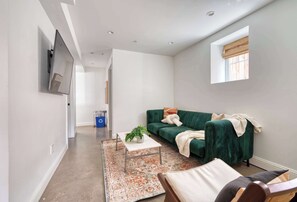 A modern living room with a green sofa, a coffee table with a plant, and a large window with a view.