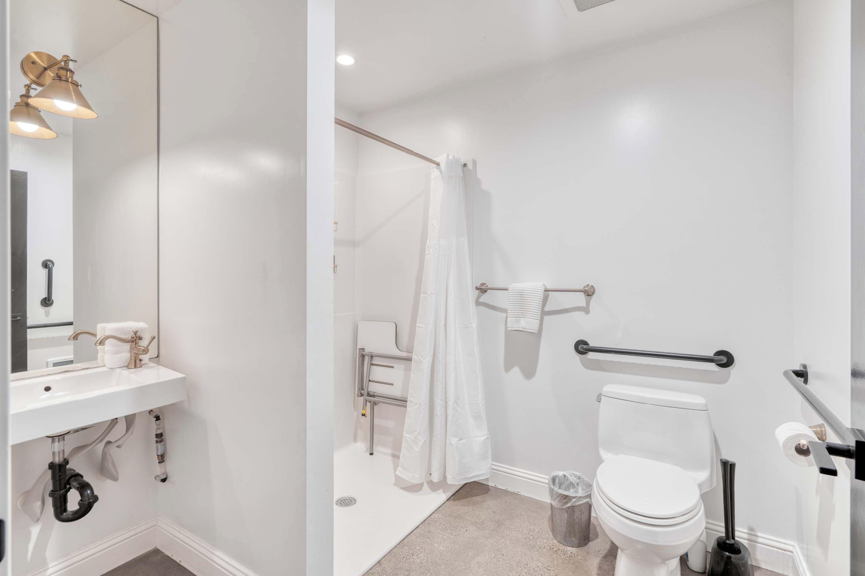 A bathroom with a white sink, mirror, toilet, and shower area.
