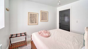 A bedroom with a bed, a wooden rack, two framed pictures, and a door. - 1906 3BR Retreat • NW 23rd Boutiques & Eats (Portland)