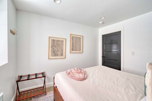 A bedroom with a bed, a wooden rack, two framed pictures, and a door.