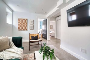 A living room with a green sofa, a wooden chair, a large flat-screen TV, and a plant on a coffee table. - 1906 3BR Retreat • NW 23rd Boutiques & Eats (Portland)