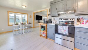 A modern kitchen with grey cabinets, a stainless steel stove, and a wooden bar stool area. - Houghton Lake Cottage w/ Patio: Walk to Waterfront (Houghton Lake)