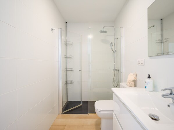 A modern bathroom with a glass-enclosed shower, a white toilet, and a sink with a mirror above it.