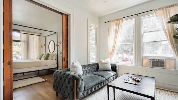 Un salon moderne avec un canapé gris, une table basse et une grande fenêtre agrémentée de rideaux.