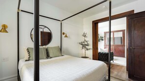Un lit à baldaquin avec une couette blanche, un miroir rond accroché au mur et une plante en pot placée à côté du lit.