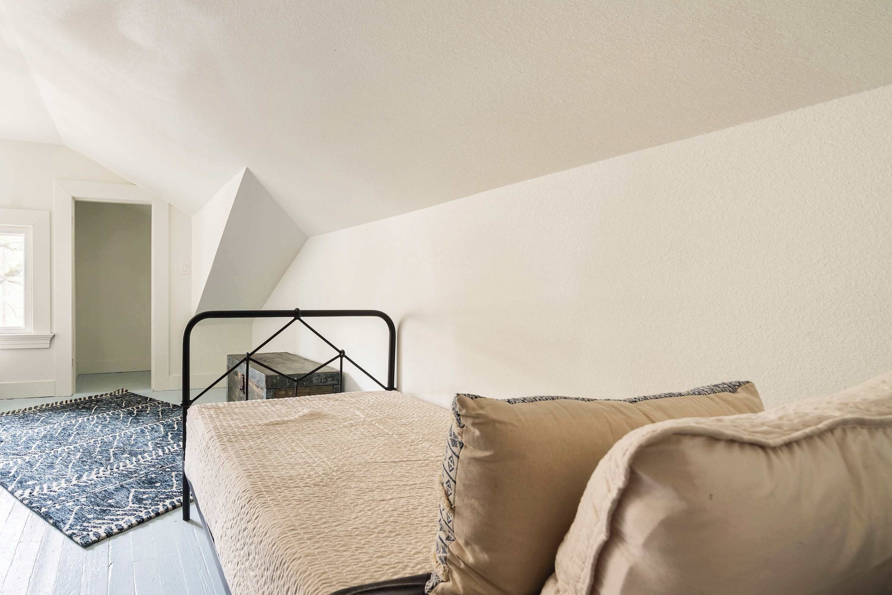 A bedroom with a bed, a hanging chair, a patterned rug, and a view of a hallway.