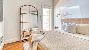 A bedroom with a large bed, a mirror, a bedside table with a lamp, and a view of the outside. - 1BR • Fast WiFi • Walk to Dining & Breweries (Portland)