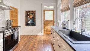A modern kitchen with a stainless steel range, wooden flooring, a large window with blinds, and a door leading to another room. - 1BR - Boutique Flat - Prime NW Location (Portland)