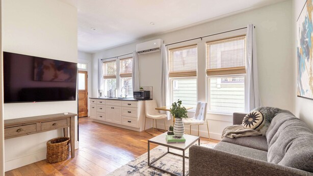 A modern living room with a flat-screen TV, a sofa, a coffee table, and a kitchen area with a microwave. - 1BR - Boutique Flat - Prime NW Location (Portland)