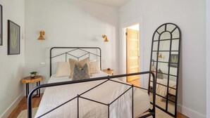 A bedroom with a metal bed frame, a bedside table with a lamp, a mirror, and a door leading to another room. - 1BR - Boutique Flat - Prime NW Location (Portland)