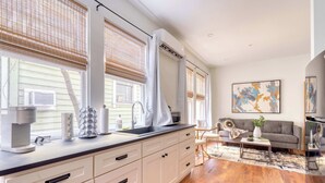A modern kitchen with a large island, white cabinetry, and a coffee machine. There is a dining area with a sofa and a coffee table. - 1BR - Boutique Flat - Prime NW Location (Portland)
