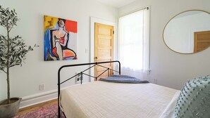 Un dormitorio con cama, planta en maceta, cuadro, puerta y espejo.