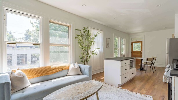 Una sala de estar moderna con sofá, mesa de centro y una zona de cocina con refrigerador y armarios.