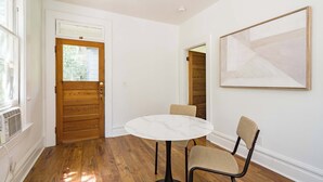 Una habitación con una mesa redonda, dos sillas, una puerta de madera y un cuadro abstracto grande en la pared.