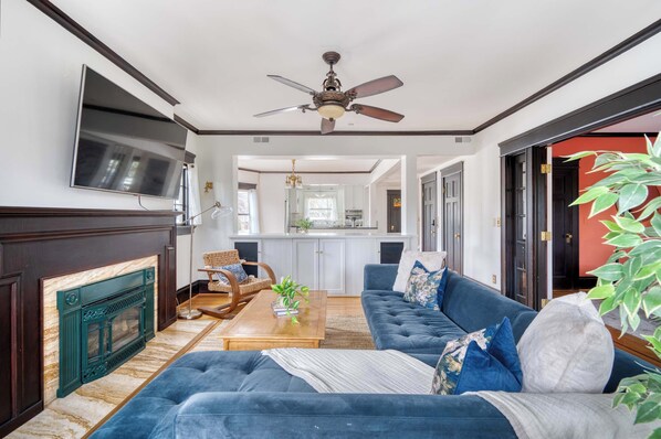 A living room with a blue sofa, a fireplace, a ceiling fan, and a TV mounted on the wall.